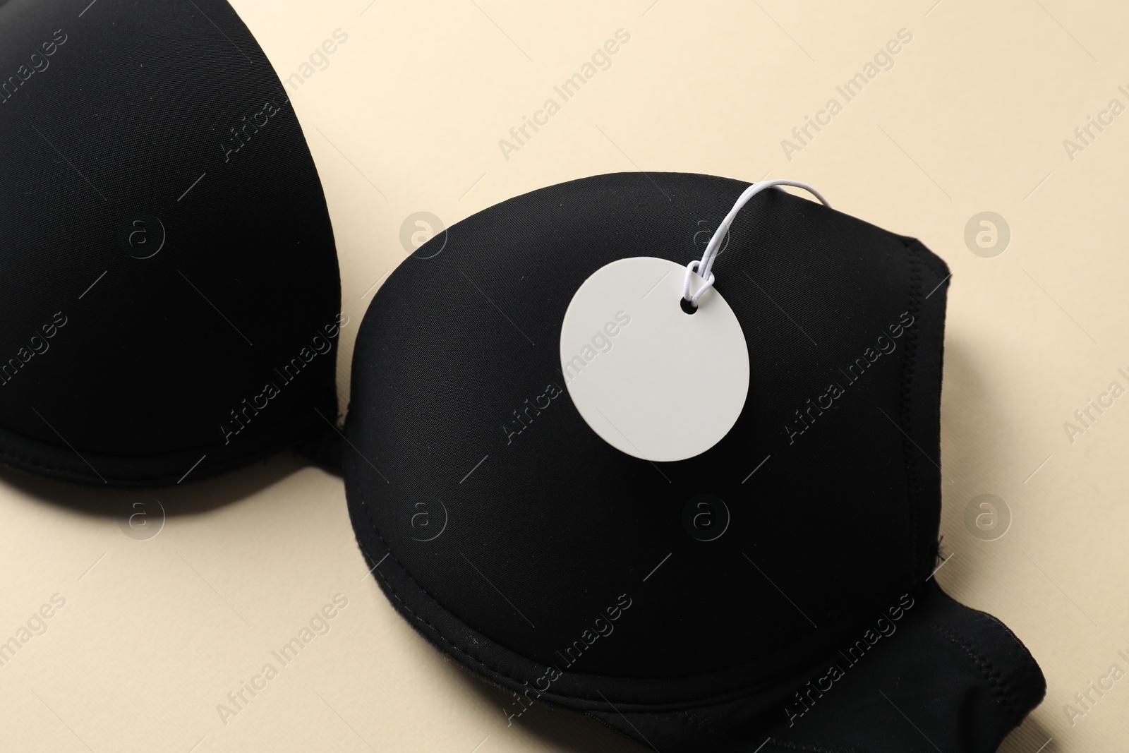 Black bra with tag on beige background, above view Photo of Black bra with tag on beige background, above view