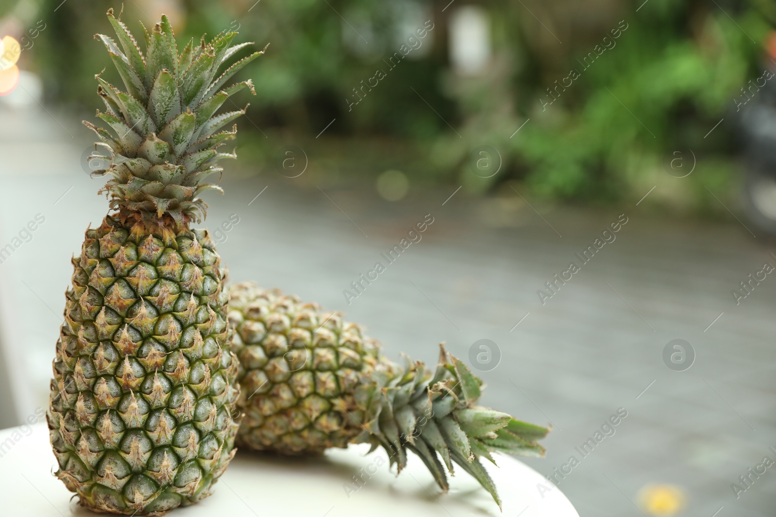 Fresh ripe pineapples on white table outdoors, closeup. Space for text Photo of Fresh ripe pineapples on white table outdoors, closeup. Space for text