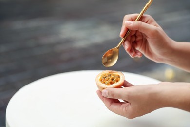 Photo of Woman eating passion fruit at table outdoors, closeup. Space for text