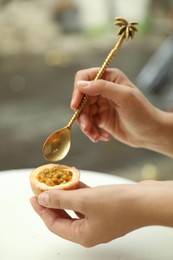 Photo of Woman eating passion fruit at table outdoors, closeup