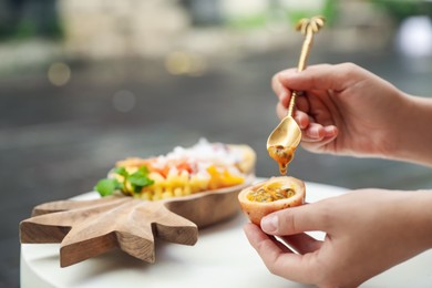 Photo of Woman eating passion fruit at table outdoors, closeup