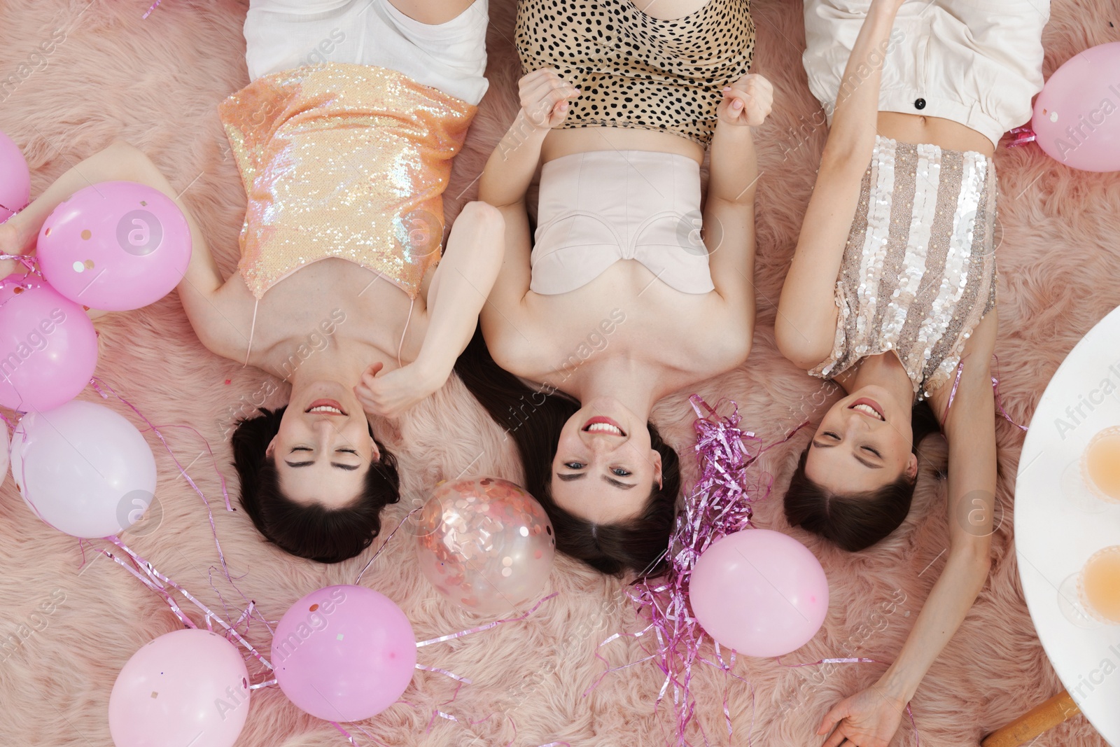 Happy friends with balloons and tinsel on faux fur, top view Photo of Happy friends with balloons and tinsel on faux fur, top view