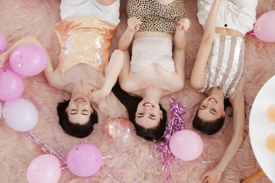 Photo of Happy friends with balloons and tinsel on faux fur, top view
