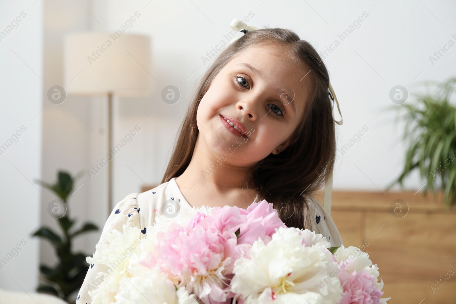Photo of Cute little girl with bouquet of beautiful peonies at home