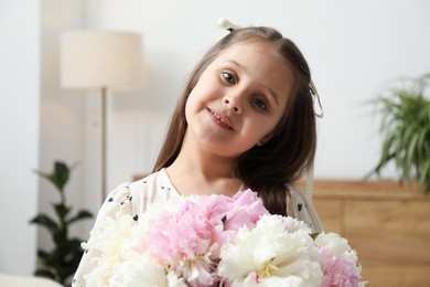 Photo of Cute little girl with bouquet of beautiful peonies at home