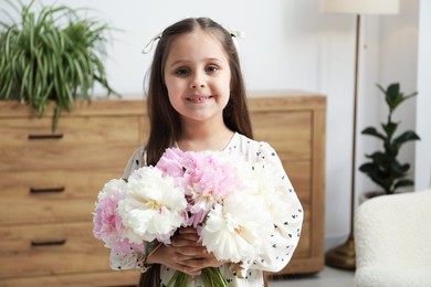 Photo of Cute little girl with bouquet of beautiful peonies at home