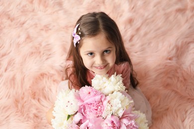 Photo of Cute little girl with bouquet of beautiful peonies on faux fur indoors, above view