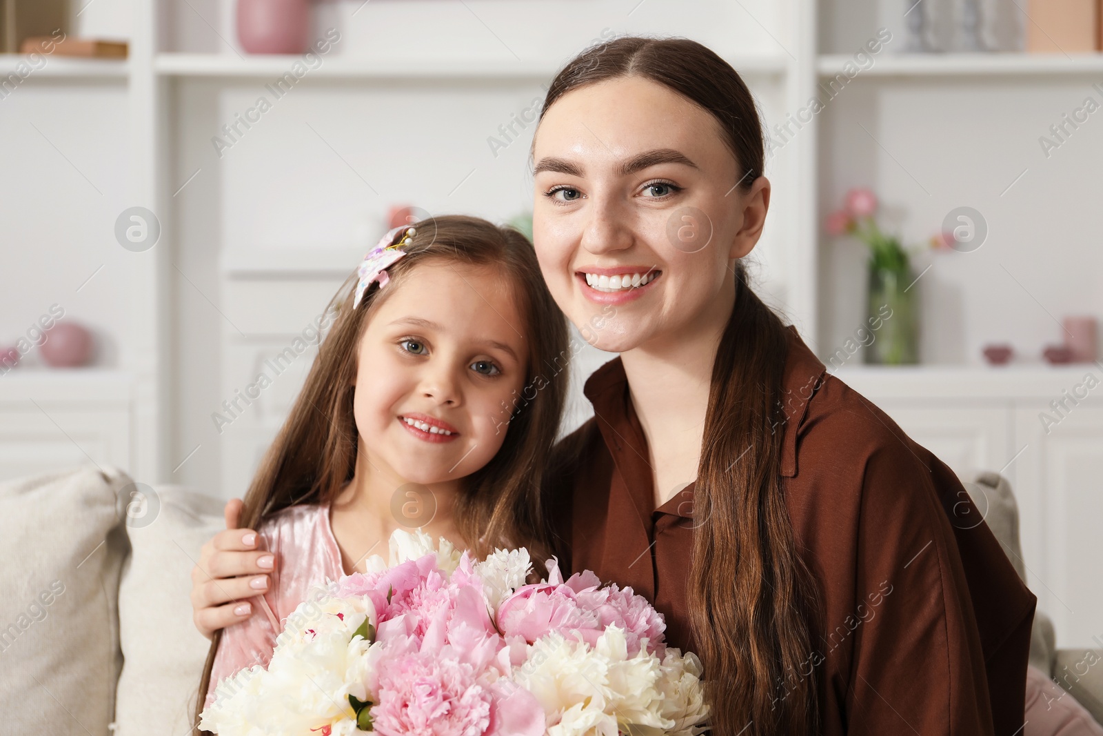 Mother and her daughter with bouquet of beautiful peonies on sofa at home Photo of Mother and her daughter with bouquet of beautiful peonies on sofa at home