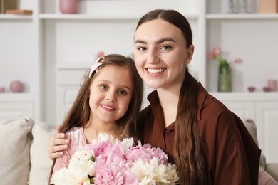 Photo of Mother and her daughter with bouquet of beautiful peonies on sofa at home