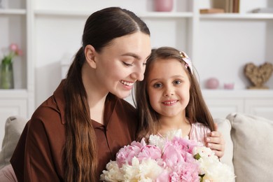 Photo of Mother and her daughter with bouquet of beautiful peonies on sofa at home