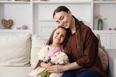 Photo of Mother and her daughter with bouquet of beautiful peonies on sofa at home