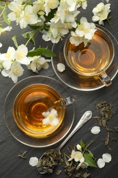 Photo of Aromatic jasmine tea, brew and flowers on grey table, flat lay