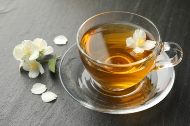 Photo of Aromatic jasmine tea and flowers on grey table, closeup