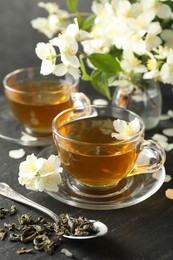 Photo of Aromatic jasmine tea, brew and flowers on grey table, closeup