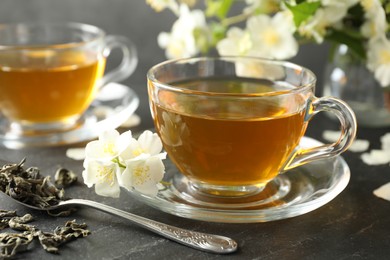 Photo of Aromatic jasmine tea, brew and flowers on grey table, closeup