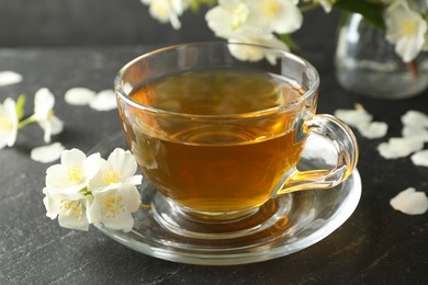 Photo of Aromatic jasmine tea and flowers on grey table, closeup