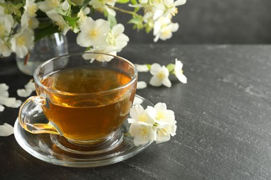 Photo of Aromatic jasmine tea and flowers on grey table, closeup. Space for text