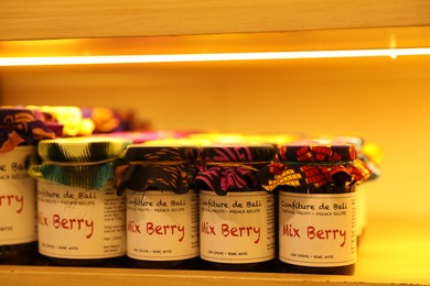 Photo of Bali, Indonesia - May 15, 2025: Different tasty jams in jars on shelf indoors, closeup