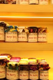 Photo of Bali, Indonesia - May 15, 2025: Different tasty jams in jars on shelves indoors, closeup