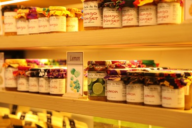 Photo of Bali, Indonesia - May 15, 2025: Different tasty jams in jars on shelves indoors, closeup