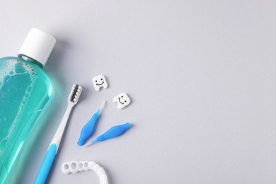Photo of Different oral care products and teeth models on light grey background, flat lay. Space for text