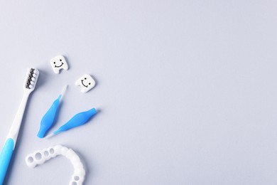 Photo of Different oral care products and teeth models on light grey background, flat lay. Space for text