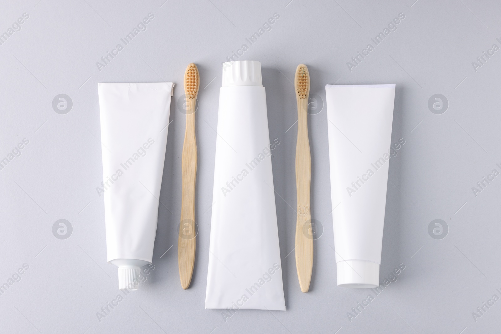 Tubes of toothpaste and toothbrushes on light grey background, flat lay Photo of Tubes of toothpaste and toothbrushes on light grey background, flat lay