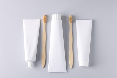 Photo of Tubes of toothpaste and toothbrushes on light grey background, flat lay