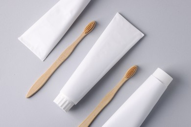 Photo of Tubes of toothpaste and toothbrushes on light grey background, flat lay
