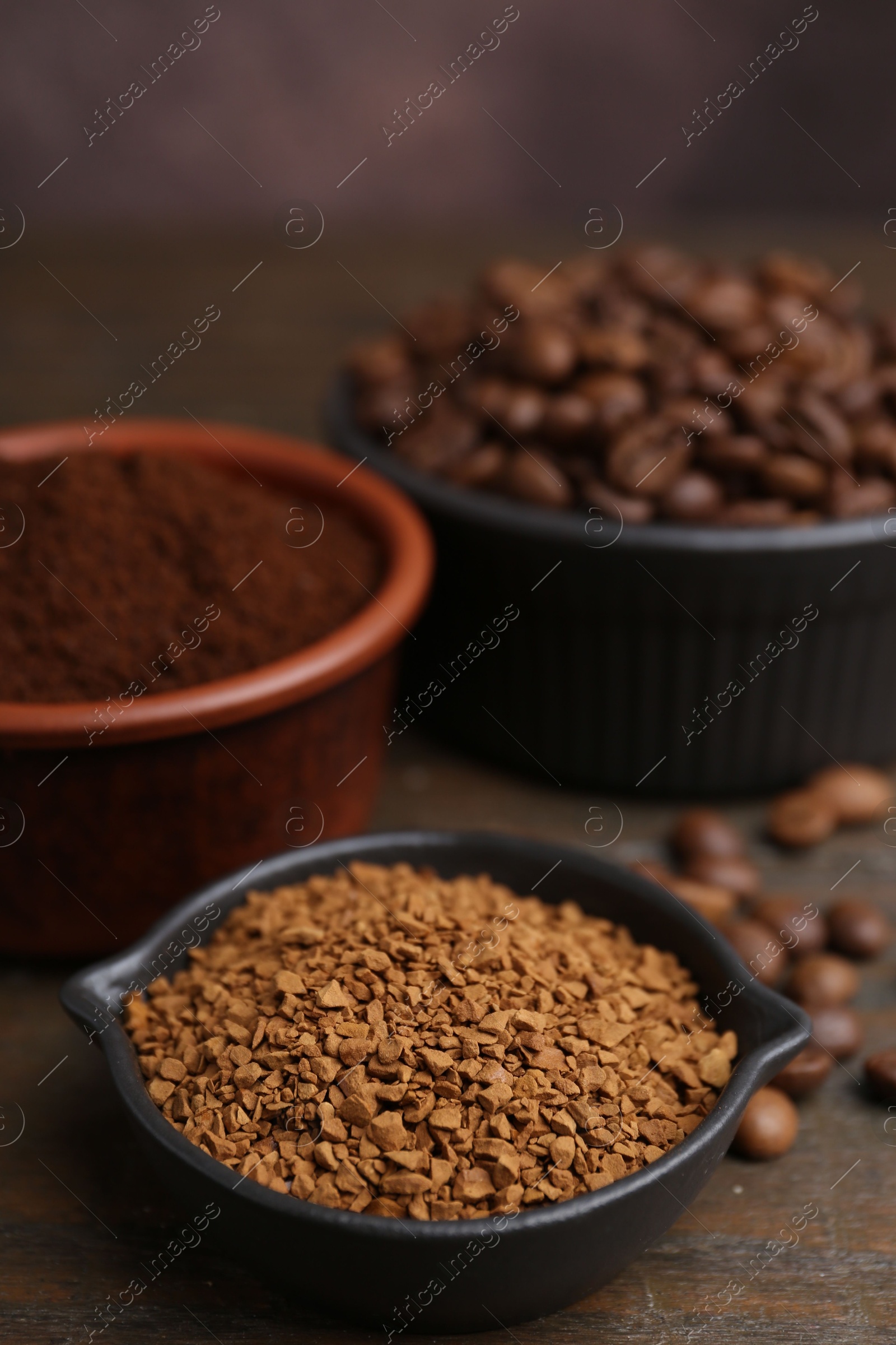 Different types of instant coffee and beans in bowls on wooden table against brown background, closeup Photo of Different types of instant coffee and beans in bowls on wooden table against brown background, closeup
