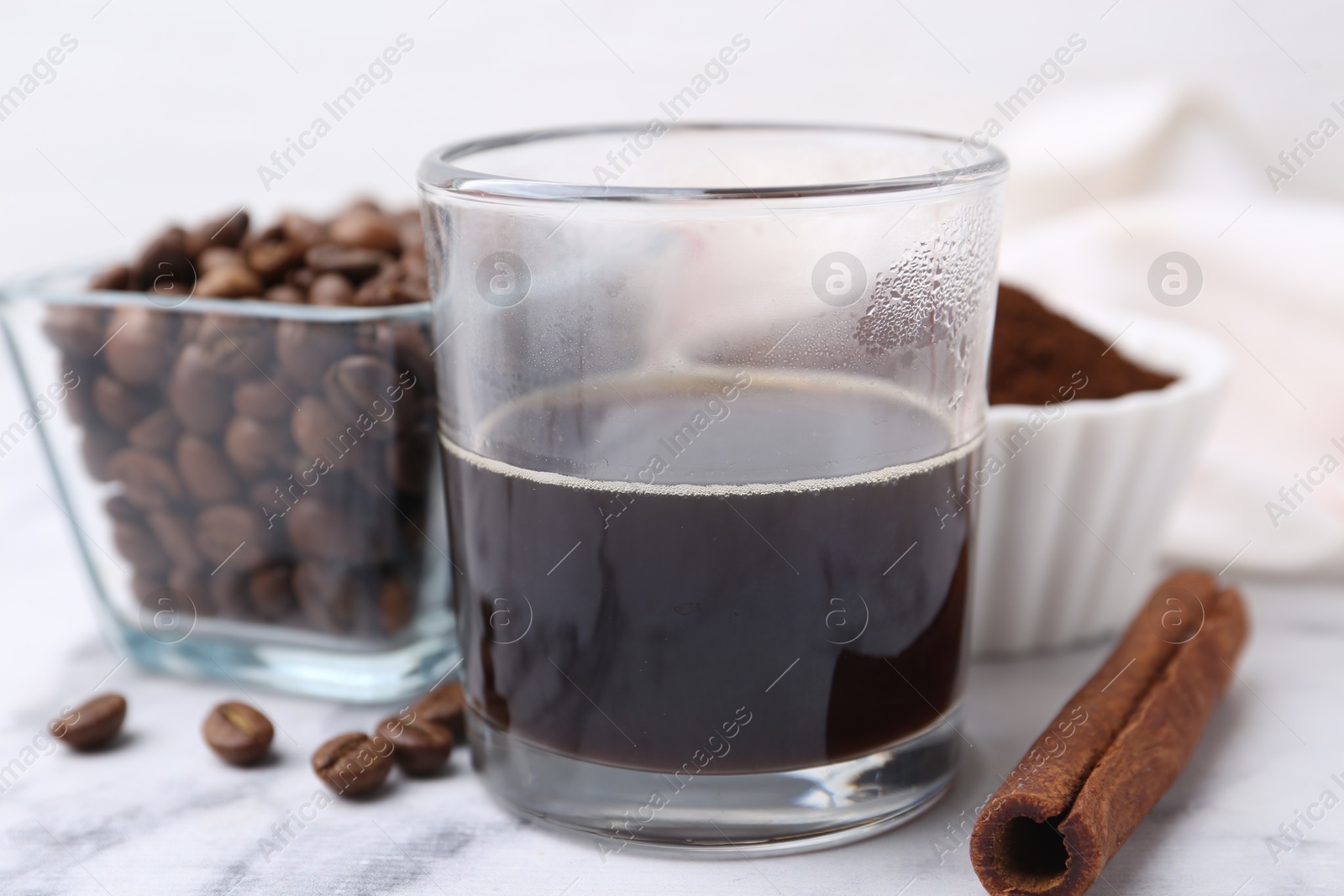 Refreshing coffee in cup, cinnamon stick and beans on white marble table, closeup Photo of Refreshing coffee in cup, cinnamon stick and beans on white marble table, closeup