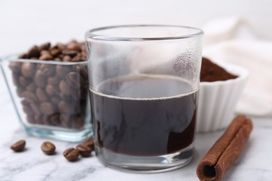 Photo of Refreshing coffee in cup, cinnamon stick and beans on white marble table, closeup