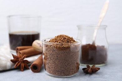 Photo of Granulated instant coffee in measuring cup and spices on grey table, closeup