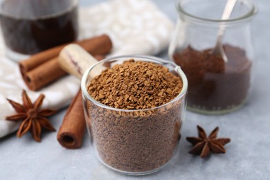 Photo of Granulated instant coffee in measuring cup and spices on grey table, closeup