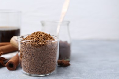 Photo of Granulated instant coffee in measuring cup and spices on grey textured table, closeup. Space for text