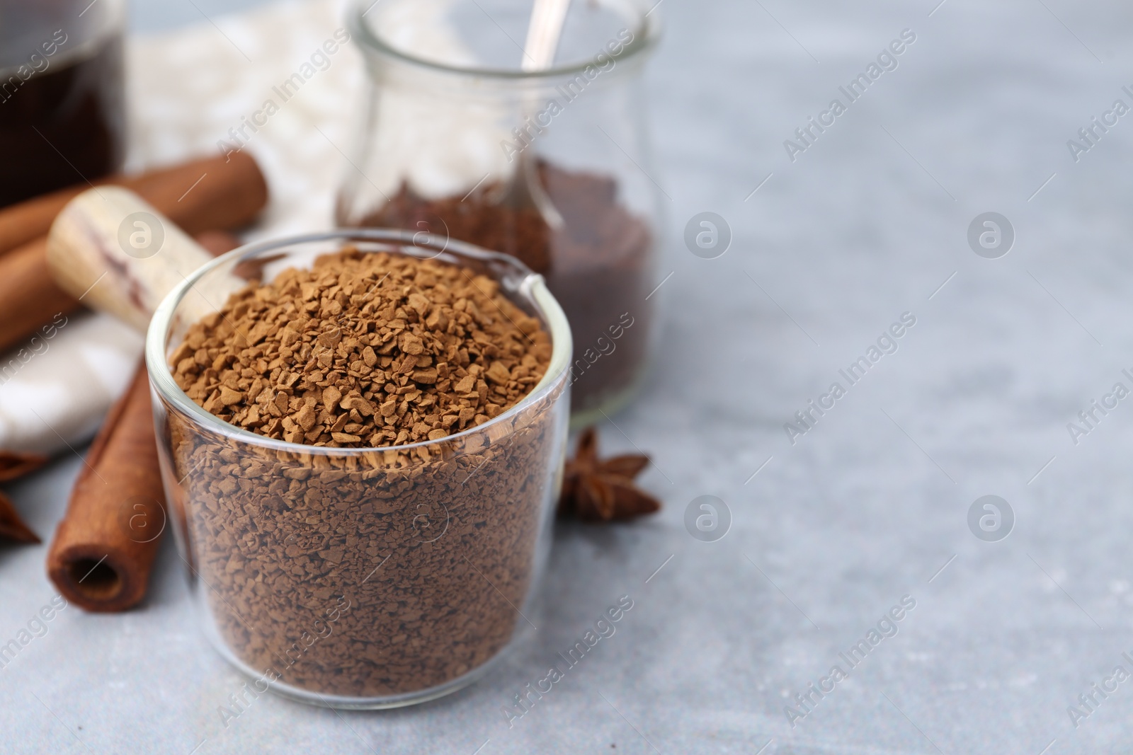 Granulated instant coffee in measuring cup and spices on grey textured table, closeup. Space for text Photo of Granulated instant coffee in measuring cup and spices on grey textured table, closeup. Space for text