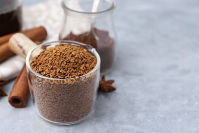 Photo of Granulated instant coffee in measuring cup and spices on grey textured table, closeup. Space for text