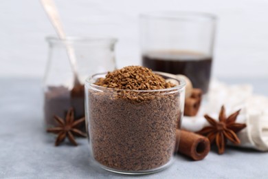 Photo of Granulated instant coffee in measuring cup and spices on grey table, closeup