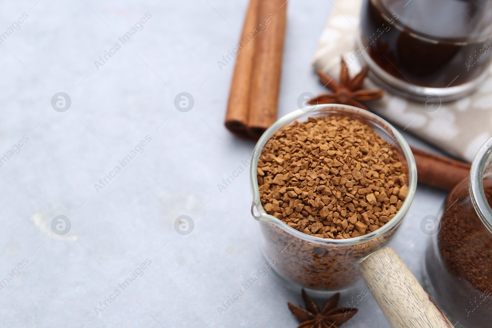 Granulated instant coffee in measuring cup and spices on grey table, closeup. Space for text Photo of Granulated instant coffee in measuring cup and spices on grey table, closeup. Space for text