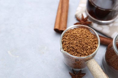 Photo of Granulated instant coffee in measuring cup and spices on grey table, closeup. Space for text