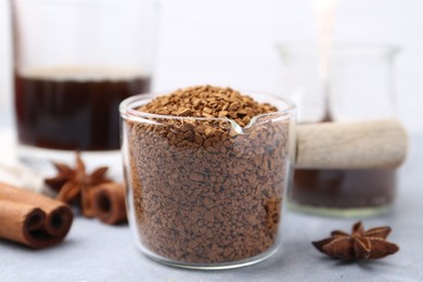 Photo of Granulated instant coffee in measuring cup and spices on grey table against light background, closeup