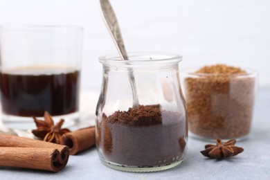 Photo of Instant coffee powder in jar and spices on grey table against light background, closeup