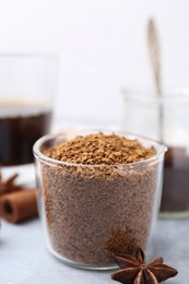Photo of Granulated instant coffee in measuring cup and spices on grey table against light background, closeup