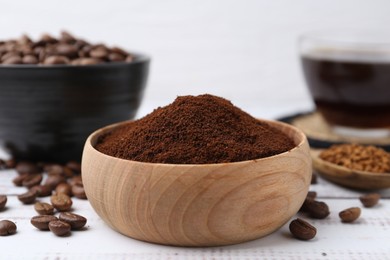 Photo of Instant coffee powder in bowl and beans on white wooden table, closeup