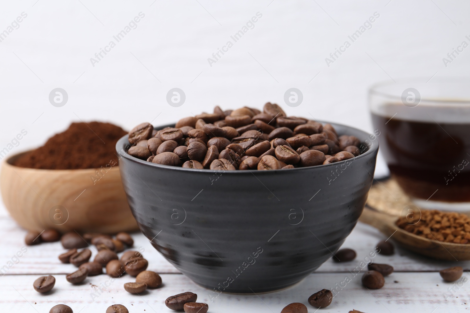 Roasted beans in bowl and different types of instant coffee on white wooden table, closeup Photo of Roasted beans in bowl and different types of instant coffee on white wooden table, closeup