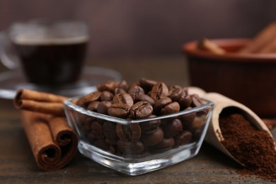 Photo of Roasted beans, instant coffee powder and cinnamon sticks on wooden table against brown background, closeup