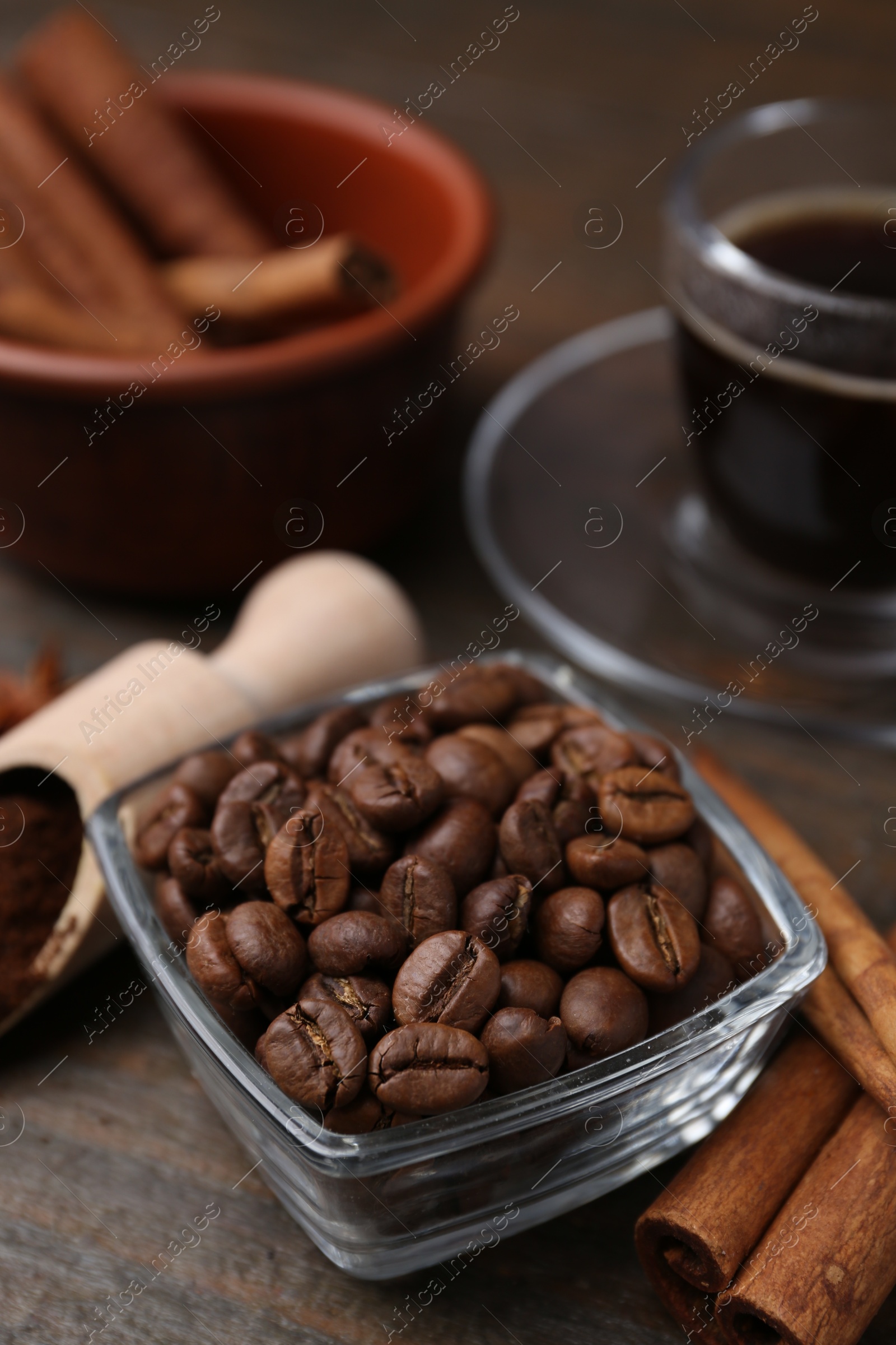 Roasted beans, scoop and cinnamon sticks on wooden table, closeup Photo of Roasted beans, scoop and cinnamon sticks on wooden table, closeup