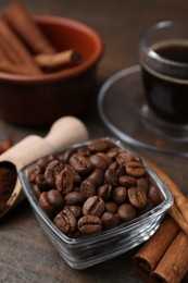 Photo of Roasted beans, scoop and cinnamon sticks on wooden table, closeup