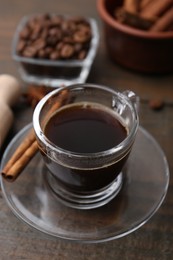 Photo of Refreshing coffee in cup and cinnamon stick on wooden table, closeup