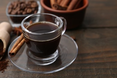 Photo of Refreshing coffee in cup and cinnamon stick on wooden table, closeup